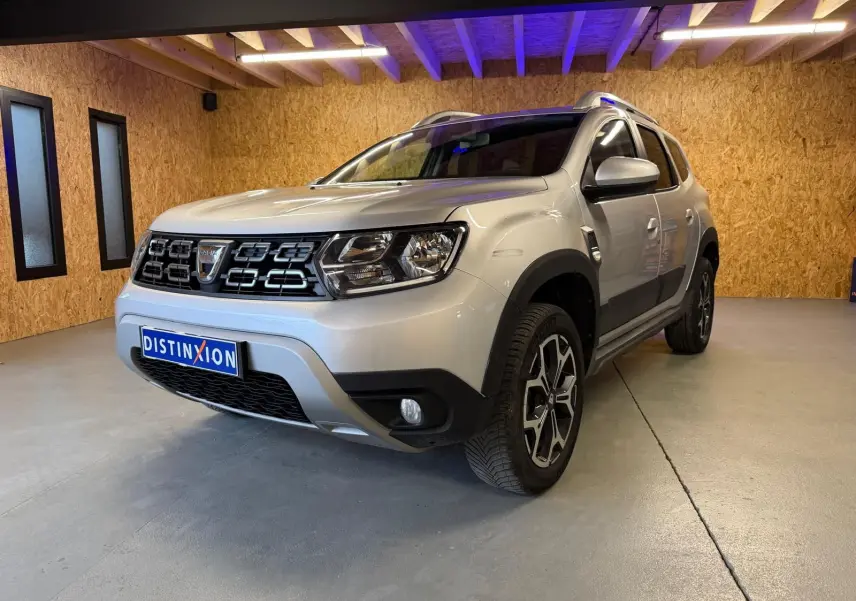 Dacia Duster gris vue 3/4 avant droit en intérieur, avec calandre noire et jantes alliage 17 pouces Maldives.