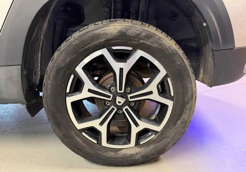 Gros plan sur la roue avant droite du Dacia Duster gris, jante alliage 17'' au design bicolore noir et argent.