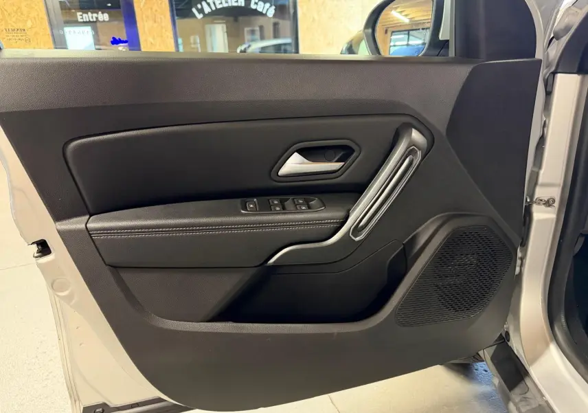 Porte avant gauche ouverte d'un Dacia Duster gris 2019, avec commandes de vitres et poignée argentée intégrée.