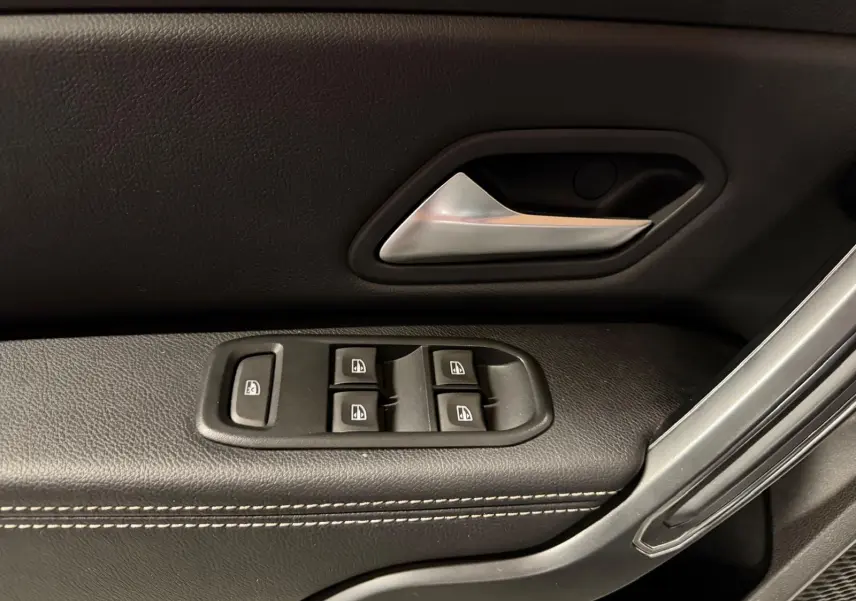 Poignée de porte intérieure noire avec surpiqûres blanches et commandes de vitres électriques côté conducteur d'un Dacia Duster gris.