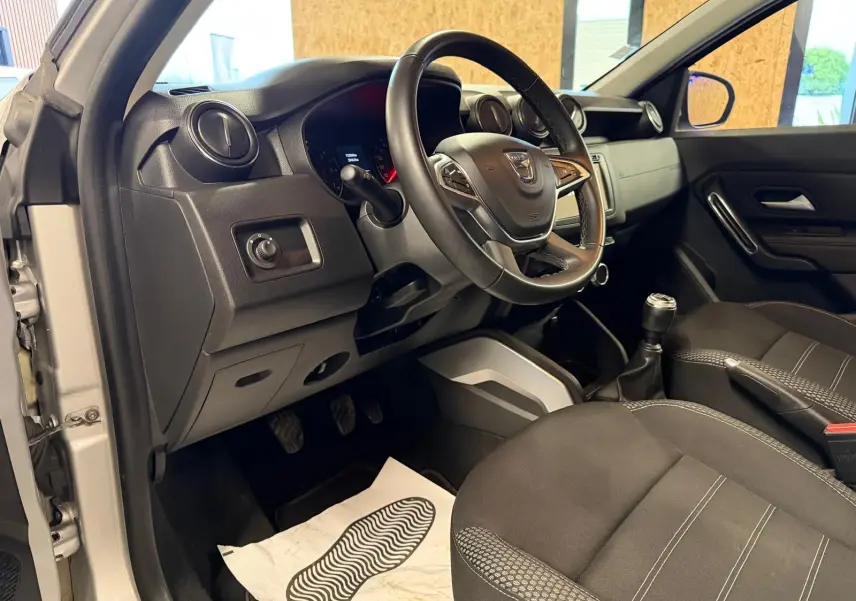 Intérieur côté conducteur du Dacia Duster gris 2019, volant, levier de vitesse et sièges tissu Prestige visibles.