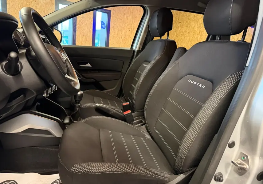 Intérieur côté conducteur du Dacia Duster gris 2019, sièges tissu noir avec logo DUSTER brodé sur appuie-têtes.