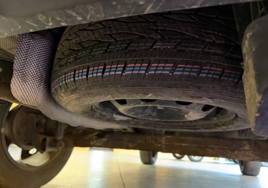 Vue sous le Dacia Duster gris 2019 montrant la roue de secours montée sur jante acier sous le châssis arrière.