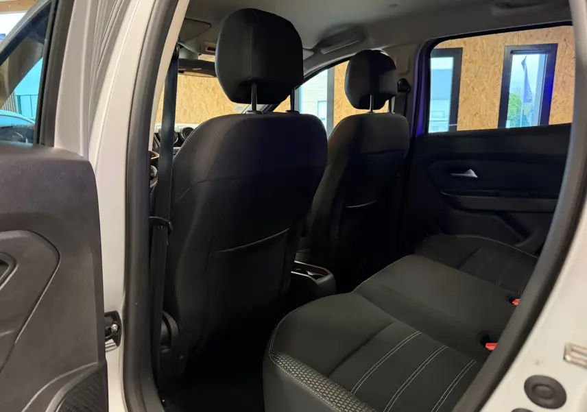 Vue intérieure arrière du Dacia Duster 2019 avec sièges tissu noir et surpiqûres blanches visibles côté droit.