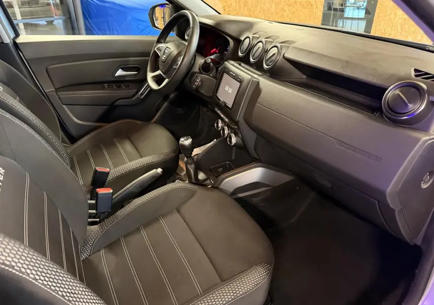 Intérieur avant droit du Dacia Duster 2019 avec sellerie tissu noire, tableau de bord épuré et volant multifonction.