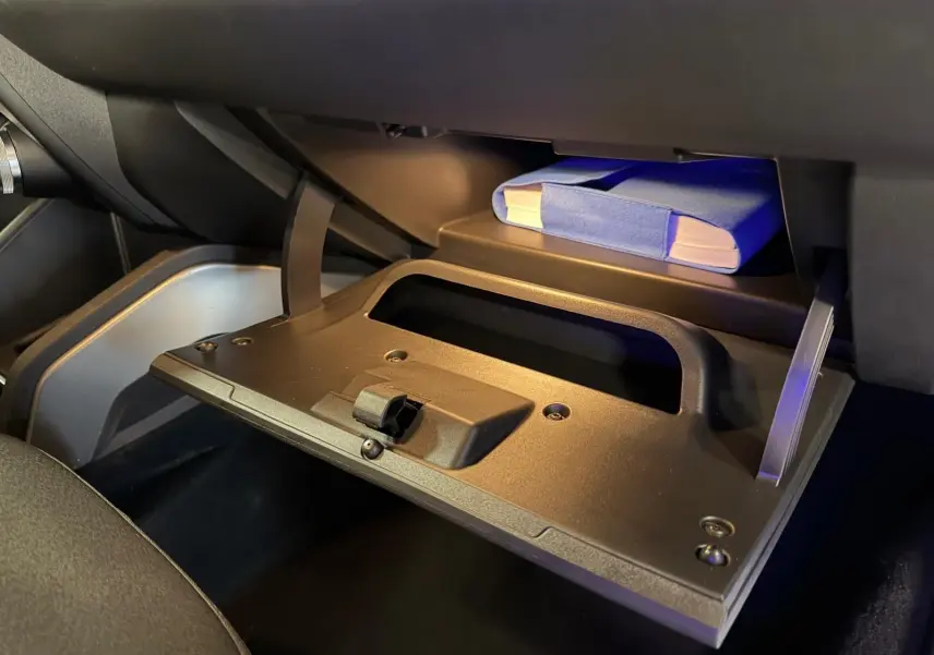 Gros plan sur la boîte à gants ouverte du Dacia Duster gris 2019, avec un manuel bleu visible à l'intérieur.