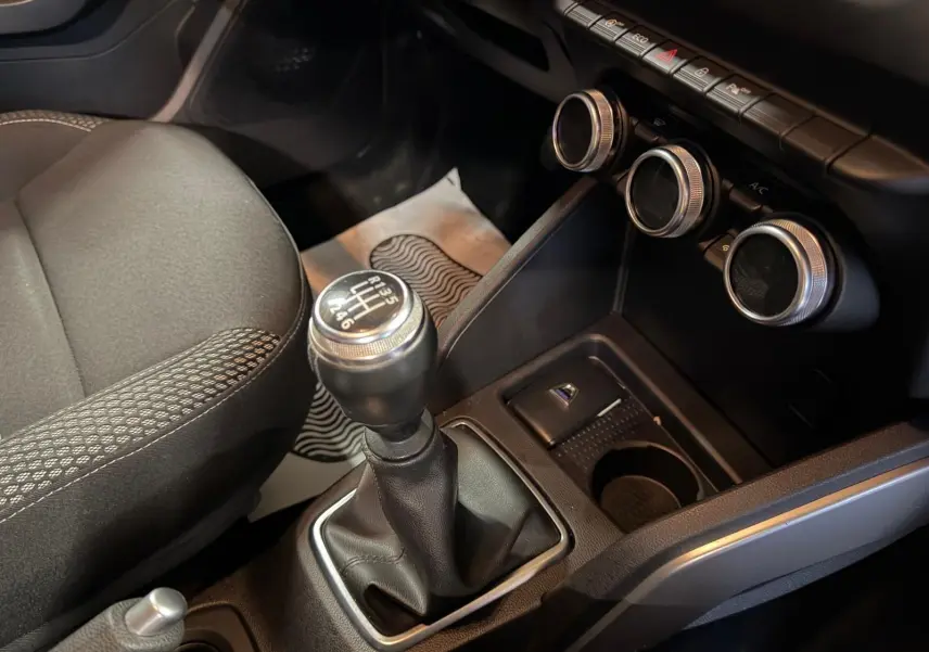 Gros plan sur la commande de boîte manuelle et la console centrale du Dacia Duster gris, avec commandes de climatisation rondes.