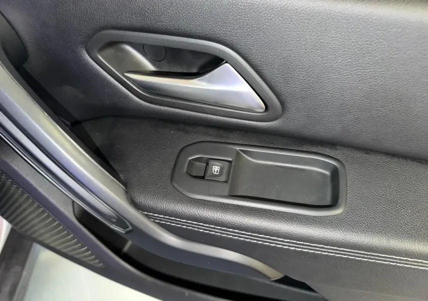 Gros plan sur la commande de lève-vitre électrique et la poignée intérieure chromée côté conducteur du Dacia Duster gris.
