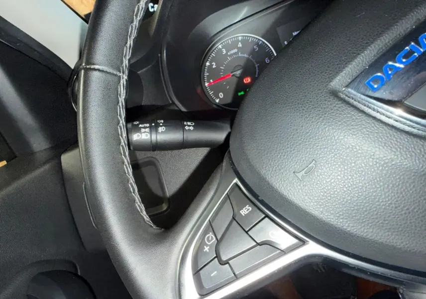 Gros plan sur le volant noir avec commandes intégrées du Dacia Duster gris 2019, tableau de bord en arrière-plan.