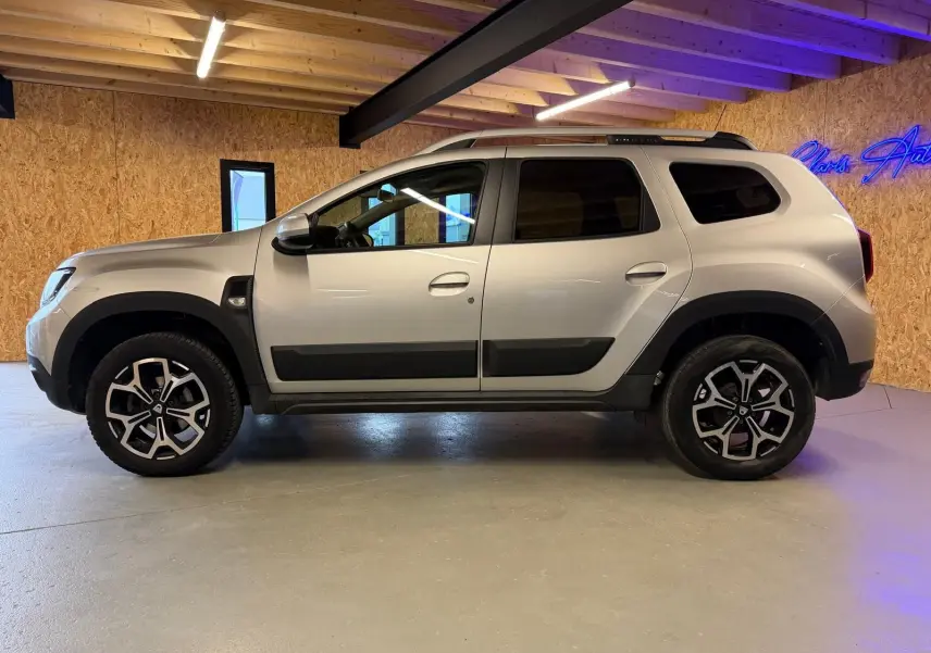 Profil côté gauche du Dacia Duster gris 2019 avec jantes alliage 17'' Maldives et protections noires sur les portes.
