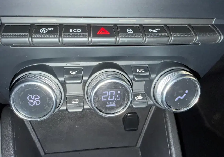 Gros plan sur les commandes de climatisation automatique du Dacia Duster gris, avec affichage digital à 20,5°C.