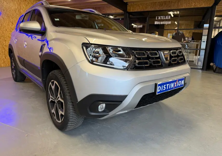 Dacia Duster gris vue 3/4 avant droit, avec calandre noire et jantes alliage 17 pouces Maldives visibles.