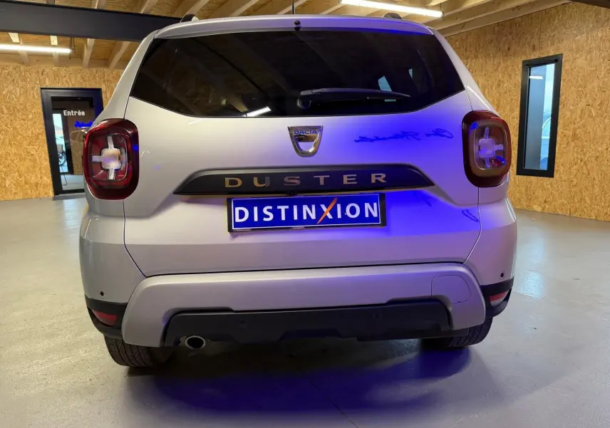 Vue arrière d'un Dacia Duster gris 2019 avec feux arrière carrés et plaque Distinxion dans un garage.