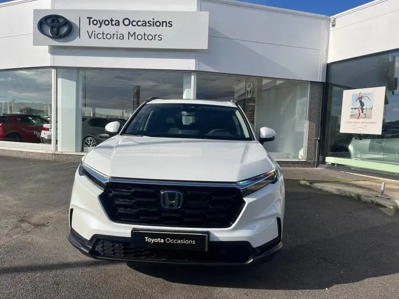 Vue avant d'un Honda CR-V blanc perle avec calandre noire, garé devant un concessionnaire Toyota Occasions.