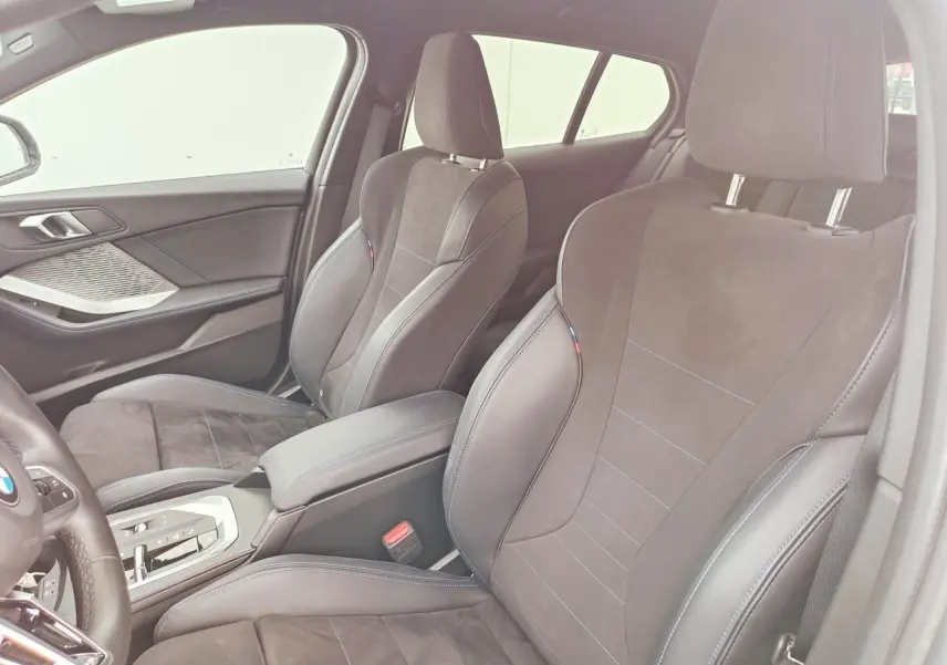 Vue intérieure côté droit sur les sièges sport Alcantara noirs avec surpiqûres bleues et accoudoir central de la BMW Série 1.