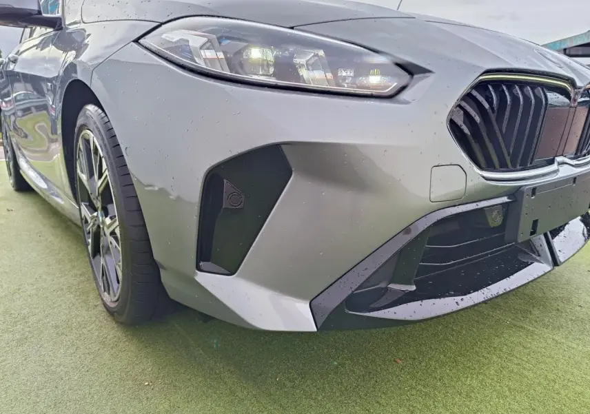 Gros plan sur l'avant droit d'une BMW Série 1 gris Skyscraper avec calandre noire et phares LED allumés.