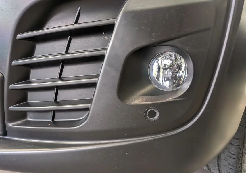 Gros plan sur le feu antibrouillard avant droit et la calandre noire du Peugeot Expert Fourgon gris acier.
