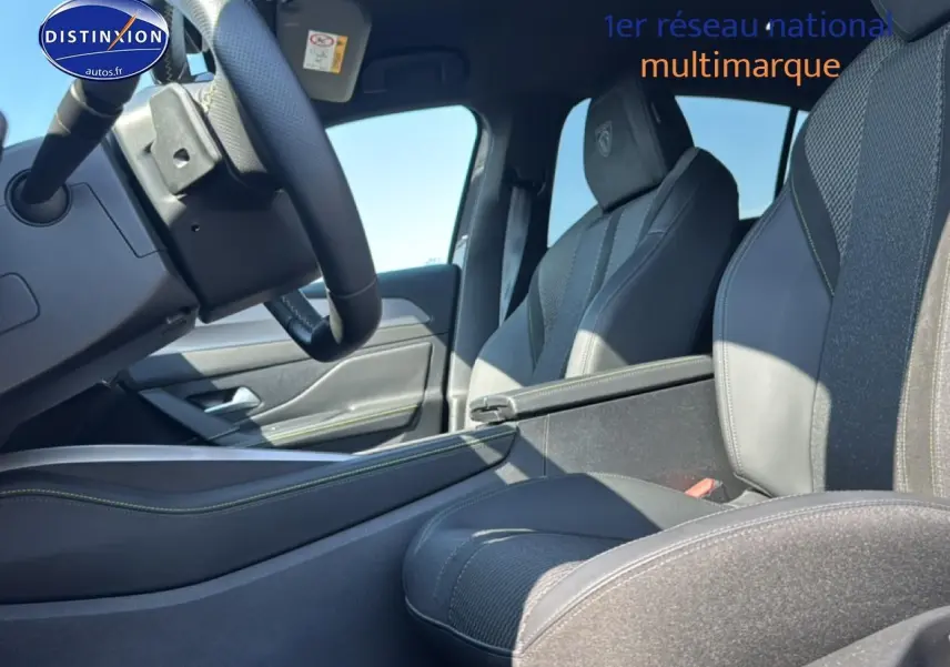 Intérieur avant droit de la Peugeot 308 gris, sièges sport avec surpiqûres vertes et accoudoir central visible.