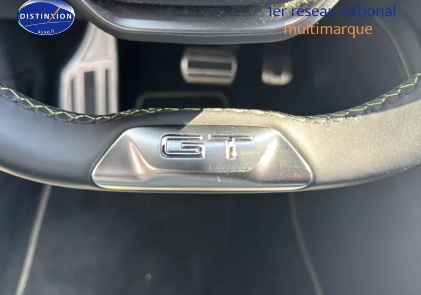 Gros plan sur le bas du volant noir avec logo GT argenté dans une Peugeot 308 gris, vue intérieure côté conducteur.