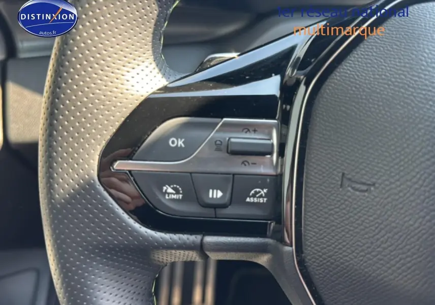Gros plan sur les commandes multifonctions à gauche du volant perforé gris d'une Peugeot 308 1.2 hybrid 145 GT 2025.