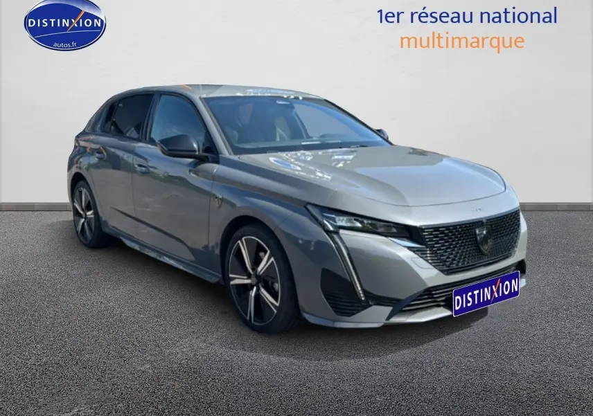 Peugeot 308 gris 3/4 avant droit, avec calandre noire et jantes alliage distinctives.