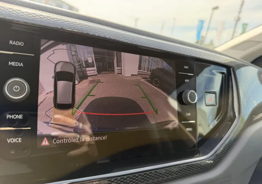 Écran tactile intérieur montrant la caméra de recul du Volkswagen Taigo bleu avec aides au stationnement activées.