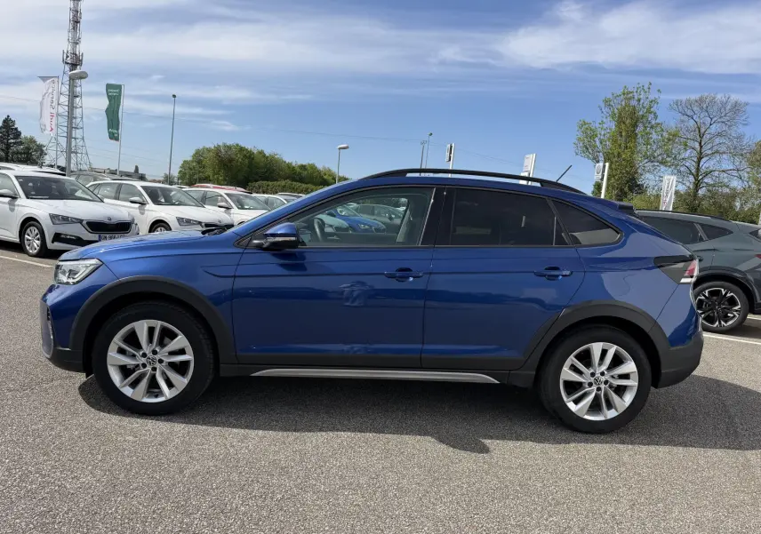 Vue de profil côté gauche d'un Volkswagen Taigo bleu métallisé avec jantes alliage 17 pouces sur un parking extérieur.