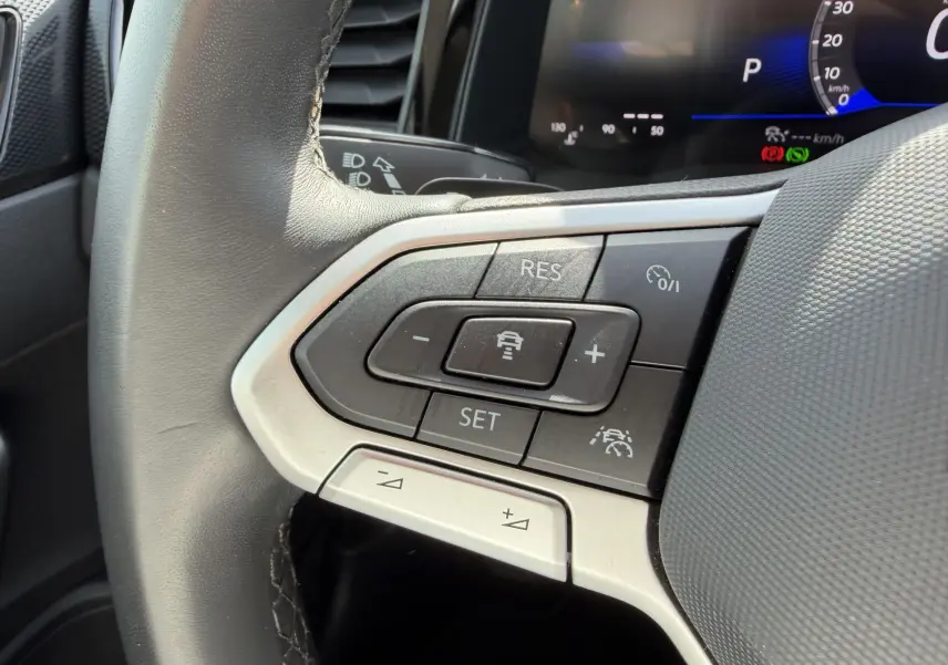 Gros plan sur les commandes multifonctions du volant cuir du Volkswagen Taigo 2025, avec affichage digital en arrière-plan.