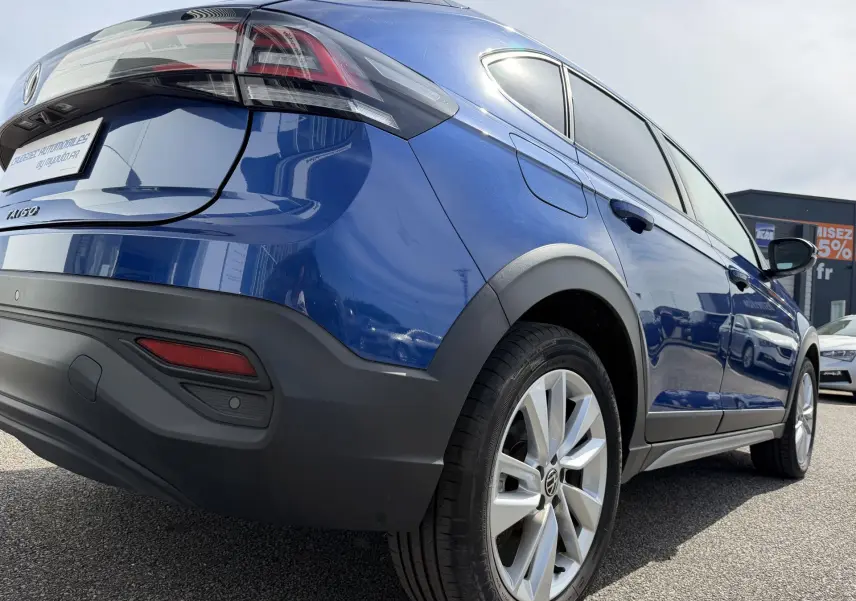 Vue 3/4 arrière droite du Volkswagen Taigo bleu métallisé avec jantes alliage et protections noires sur les passages de roues.