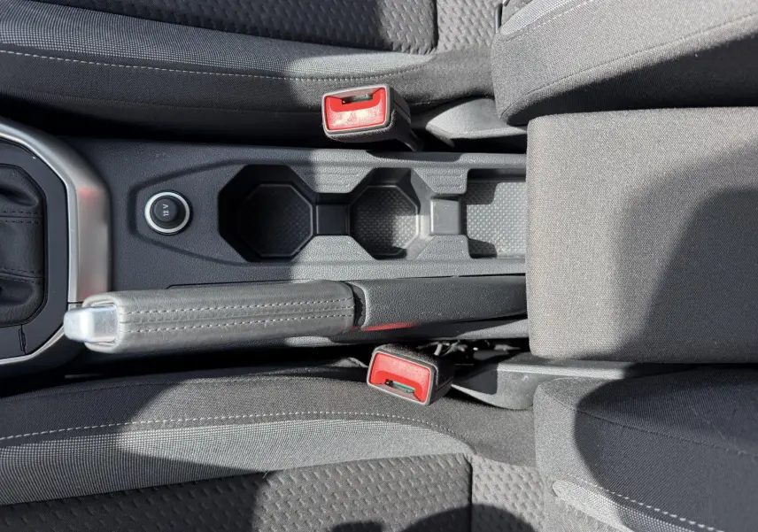 Vue plongeante sur la console centrale noire du Volkswagen Taigo avec frein à main manuel et porte-gobelets.