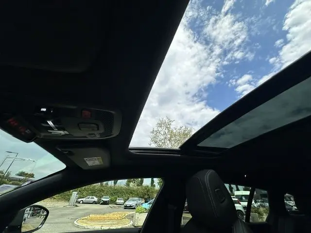 Vue intérieure du toit ouvrant panoramique du Peugeot 508 SW gris, avec ciel partiellement nuageux visible à travers le verre.