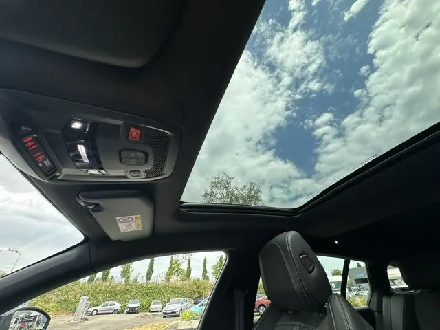 Vue intérieure du toit ouvrant panoramique et des sièges noirs du Peugeot 508 SW gris, avec ciel nuageux visible.