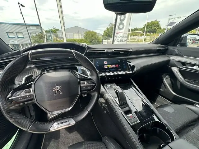 Vue intérieure de face du poste de conduite d'une Peugeot 508 SW gris, avec volant compact et écran tactile central.