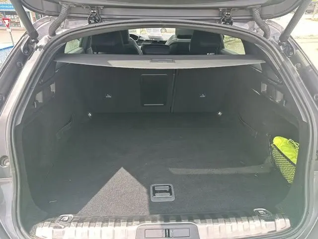 Coffre ouvert vu de l'arrière d'un Peugeot 508 SW gris 2020, espace de chargement vide avec filet latéral contenant un objet jaune.