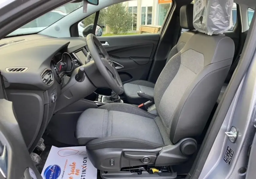Vue intérieure côté conducteur de l’Opel Crossland gris alu 2022, sièges tissu gris et tableau de bord moderne.