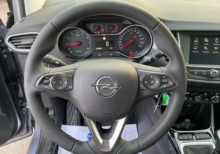 Vue rapprochée du volant multifonction d'une Opel Crossland gris alu 2022, avec tableau de bord et écran tactile visibles.