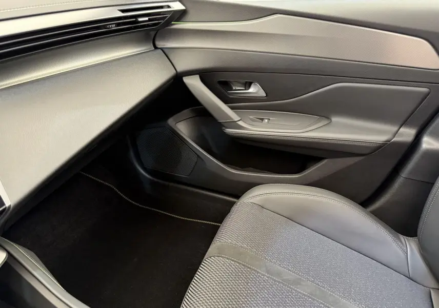 Intérieur côté passager de la Peugeot 308 Hybrid 136 e-DCS6 GT 2024 en gris foncé, avec siège et porte élégants.