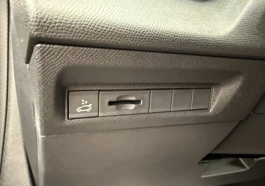 Gros plan sur le bouton d'ouverture du coffre côté gauche dans l'habitacle gris foncé du Peugeot 308 Hybrid 2024.