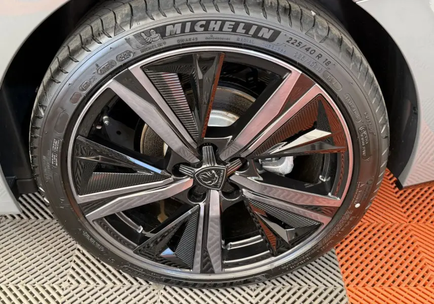 Gros plan sur la jante noire et argentée avec logo Peugeot de la roue avant droite d'une 308 Hybrid 136 e-DCS6 GT gris foncé.