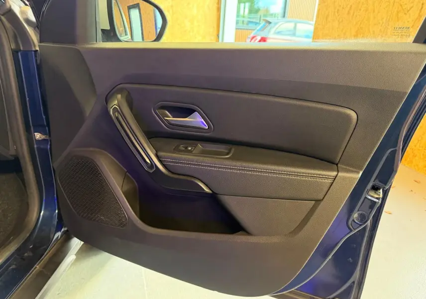 Vue intérieure de la porte avant gauche bleu foncé du Dacia Duster avec poignée et commande de vitre électrique.