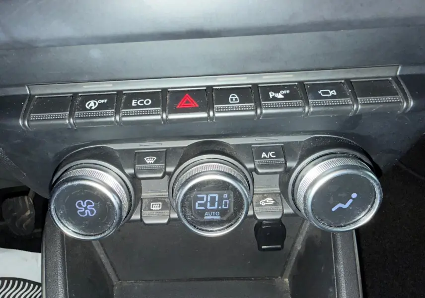 Gros plan sur la console centrale noire du Dacia Duster bleu, montrant les commandes de climatisation automatique et boutons fonctionnels.