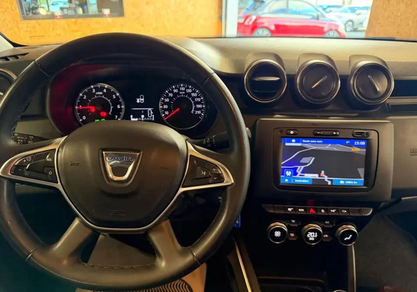 Vue frontale de l'intérieur du Dacia Duster bleu, volant cuir avec commandes, tableau de bord et écran tactile GPS.