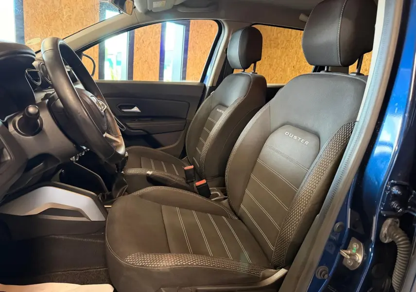Intérieur du Dacia Duster bleu, vue côté gauche sur les sièges avant en tissu "Prestige" avec logo brodé.