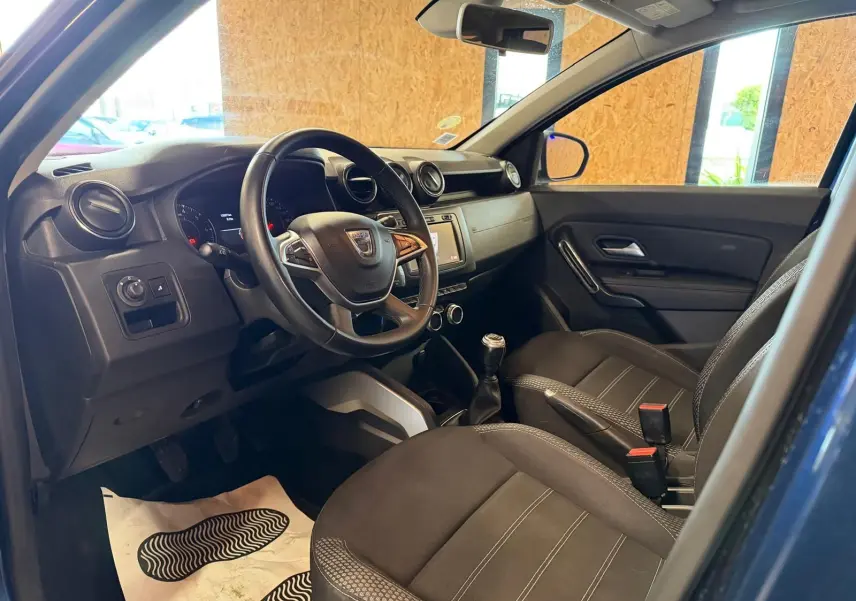 Intérieur avant droit du Dacia Duster bleu, volant multifonctions, sièges tissu Prestige et levier de vitesse manuel visible.