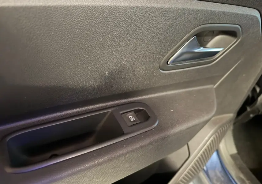 Gros plan sur la porte intérieure côté droit du Dacia Duster bleu, avec poignée argentée et bouton de lève-vitre.