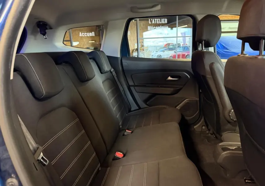 Vue intérieure côté gauche des sièges arrière noirs du Dacia Duster bleu, avec surpiqûres et appuie-têtes ajustés.