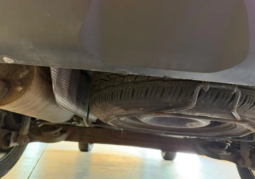 Vue sous le Dacia Duster bleu, montrant la roue de secours galette et le système d'échappement arrière.