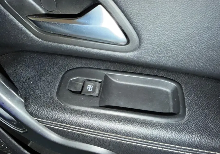 Gros plan sur la poignée intérieure et le bouton de lève-vitre côté gauche du Dacia Duster bleu Prestige.