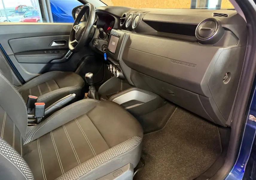 Intérieur avant droit du Dacia Duster bleu, avec tableau de bord noir, sièges tissu Prestige et volant réglable.