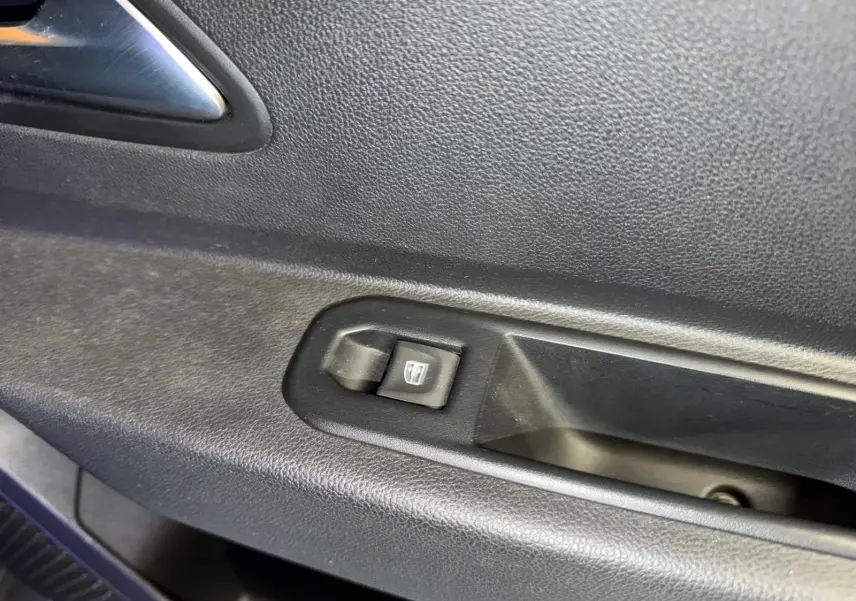 Gros plan sur le bouton de lève-vitre électrique côté gauche intérieur du Dacia Duster bleu Prestige.